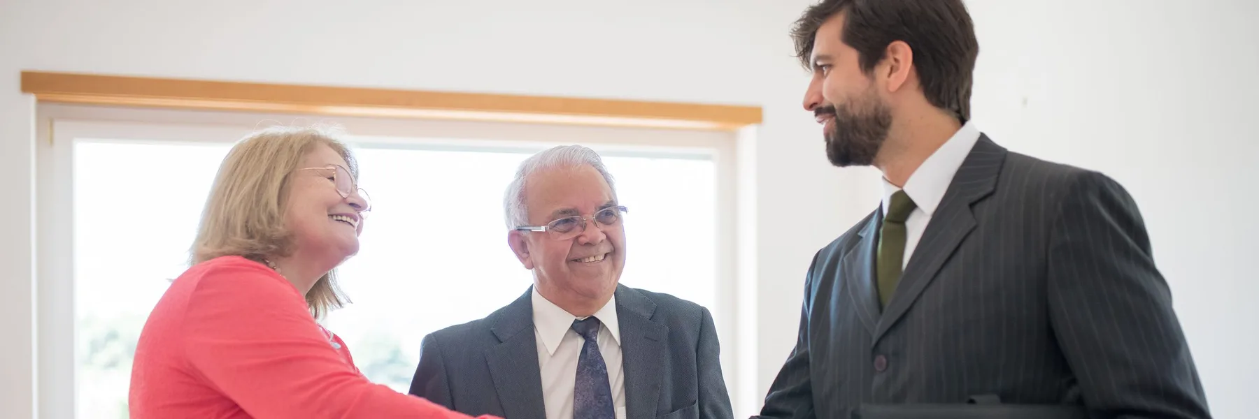 Un conseiller serre la main d’un couple de retraités autour de leur dossier